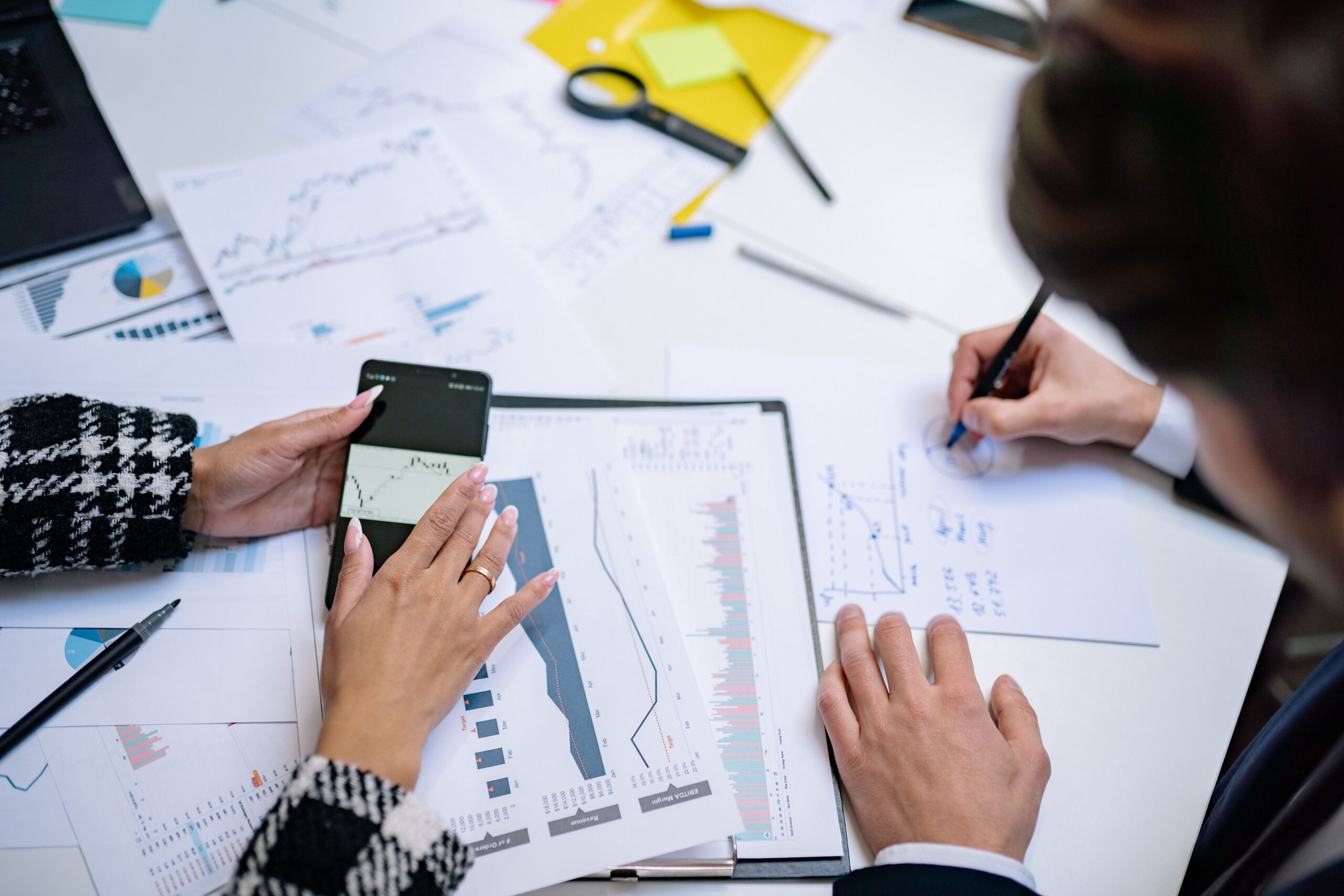 Overhead view of people analyzing financial graphs and data with smartphone and documents.