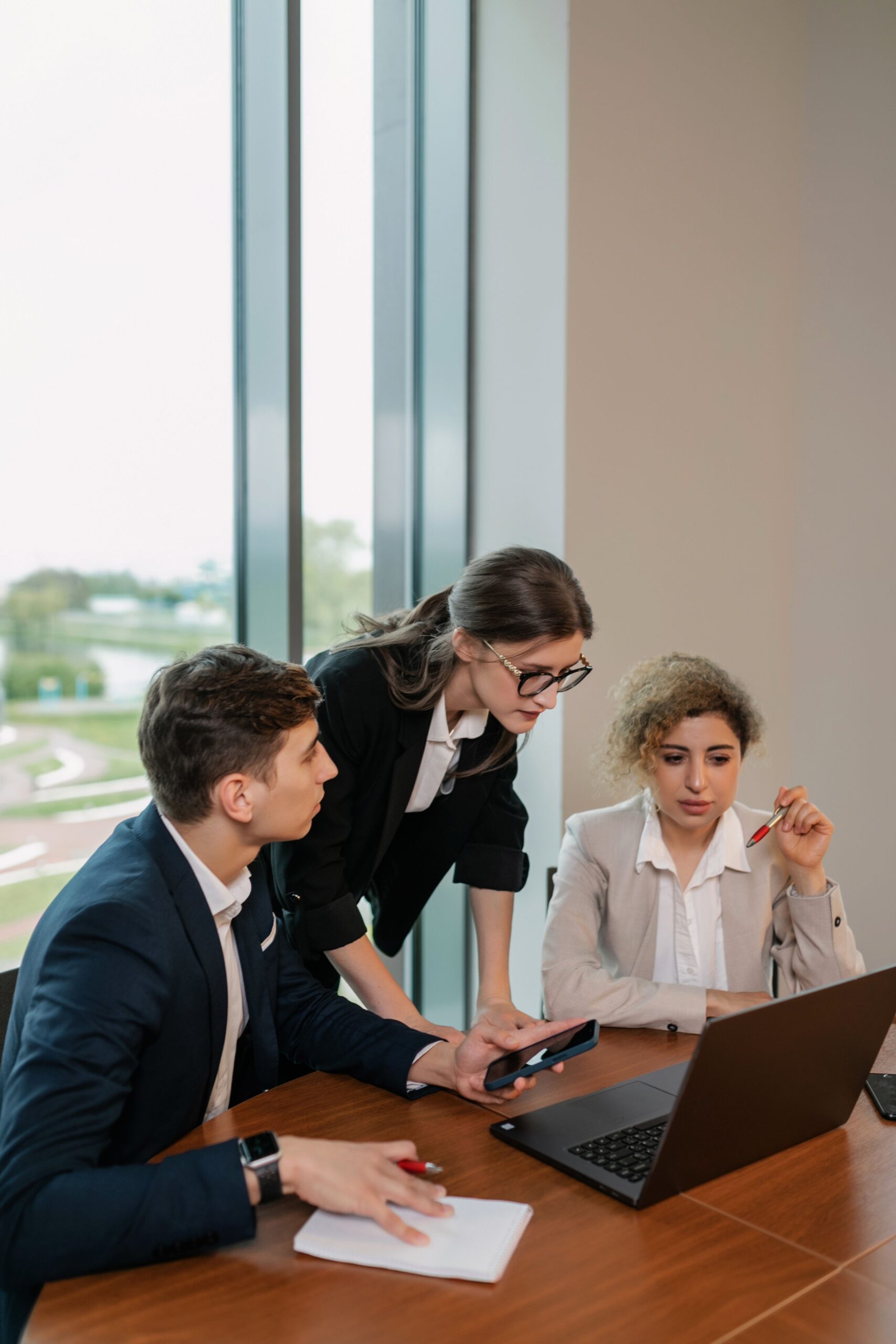Group of business professionals discussing work at a laptop in a modern office setting.
